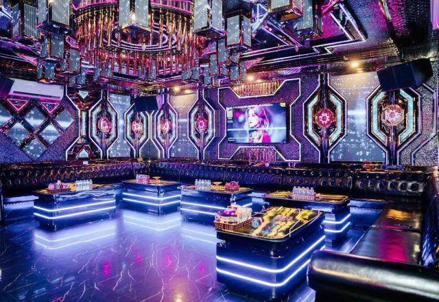 Phòng hát lớn tại Karaoke Level với dàn ghế sofa da đen, bàn viền đèn LED và tường LED tím