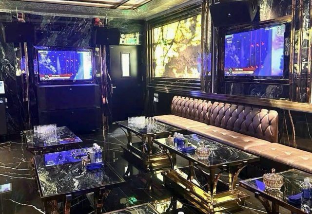 Phòng hát ốp đá vân đen tại Karaoke Level, sofa nỉ màu be, bàn khung mạ vàng, hai màn hình