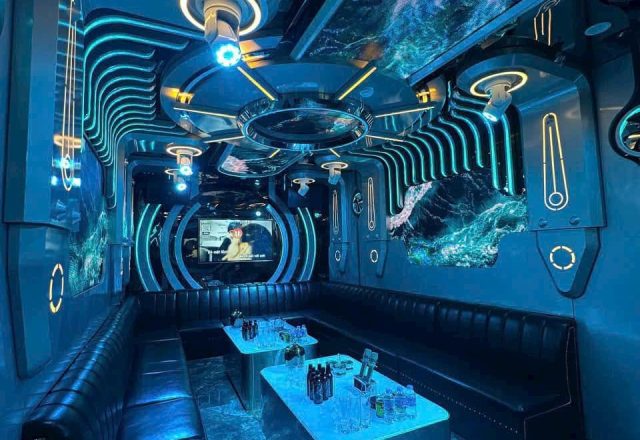 Phòng hát tại Karaoke Flamenco với đèn LED xanh, trần trang trí, sofa da đen và bàn dài