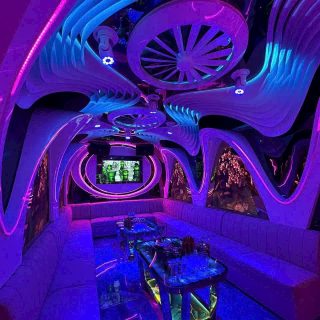 Phòng hát ở Karaoke Flamenco với trần uốn lượn, đèn neon xanh tím, sofa dài và màn hình treo tường