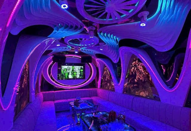 Phòng hát ở Karaoke Flamenco với trần uốn lượn, đèn neon xanh tím, sofa dài và màn hình treo tường