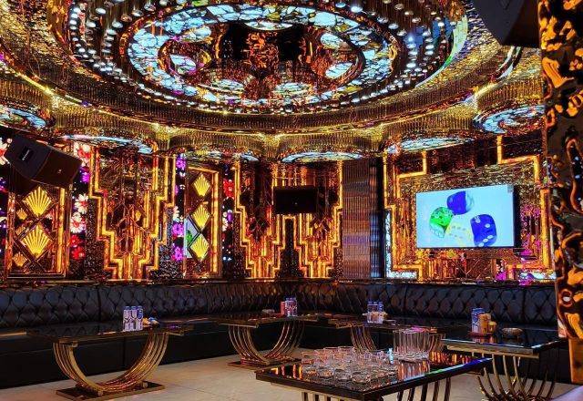 Phòng hát rộng tại Karaoke Tiptop với trần vòm mạ vàng, ghế sofa da đen, bàn chân vàng và màn hình lớn