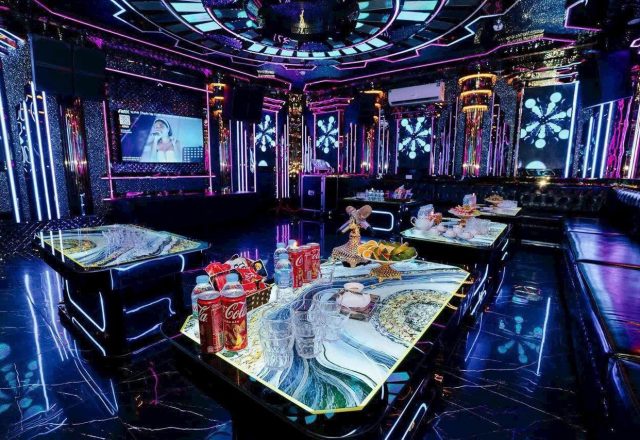 Phòng hát Karaoke Tiptop tông tím xanh, bàn kính vân đá bày ly và trái cây, sofa da tối màu