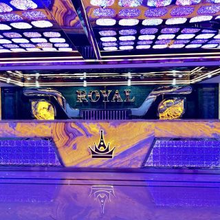Quầy lễ tân ốp đá vân vàng, logo vương miện và chữ ROYAL phát sáng dưới trần đèn tím tại Karaoke Royal 97 Cầu Giấy