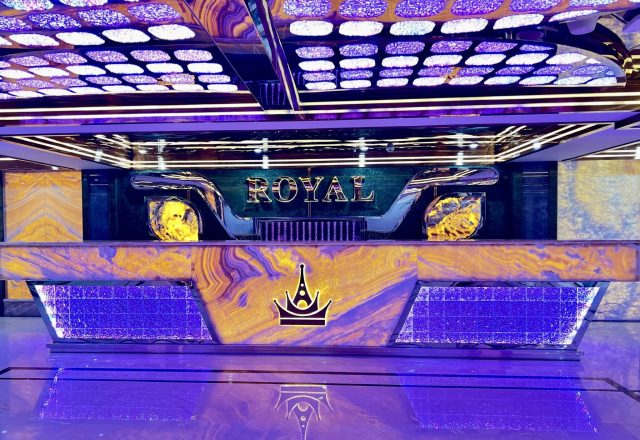 Quầy lễ tân ốp đá vân vàng, logo vương miện và chữ ROYAL phát sáng dưới trần đèn tím tại Karaoke Royal 97 Cầu Giấy