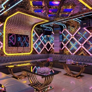 Phòng hát tại Karaoke Tiptop có tường LED hình thoi hồng xanh, sofa xám bọc nút, bàn kính chân vàng và loa treo