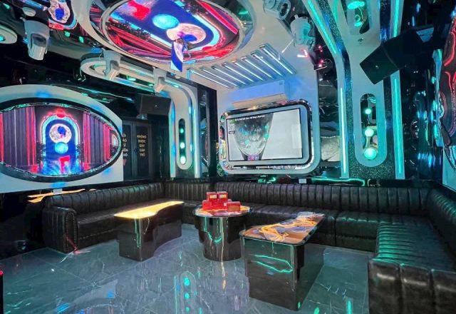 Phòng karaoke tông tối tại S KTV Club, đèn LED xanh ngọc, sofa da đen quây góc và màn hình tivi
