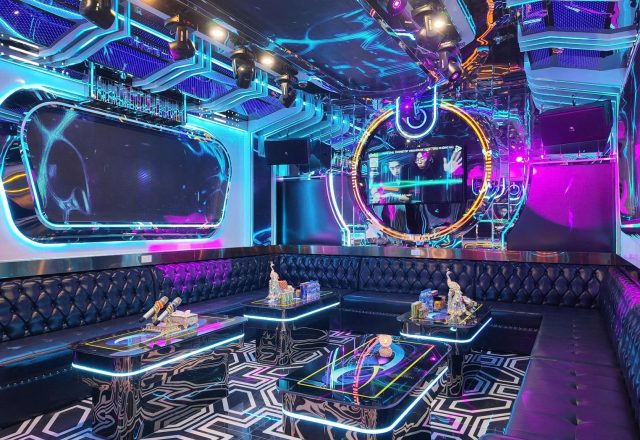 Phòng hát tại Karaoke Royal 97 Cầu Giấy với ghế sofa da đen, bàn viền đèn LED, màn hình và đèn neon xanh tím
